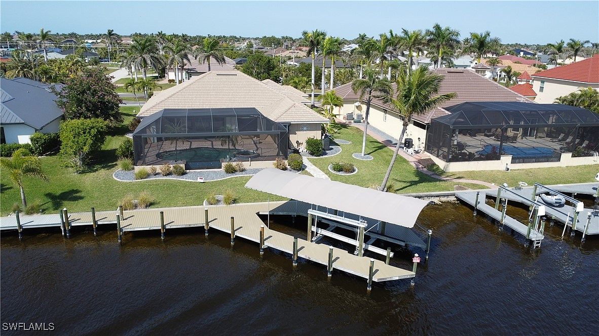 Aerial view of a Gulf Coast canal-front home with covered boat lift, composite dock, and neighboring lift alongside a wide navigable canal